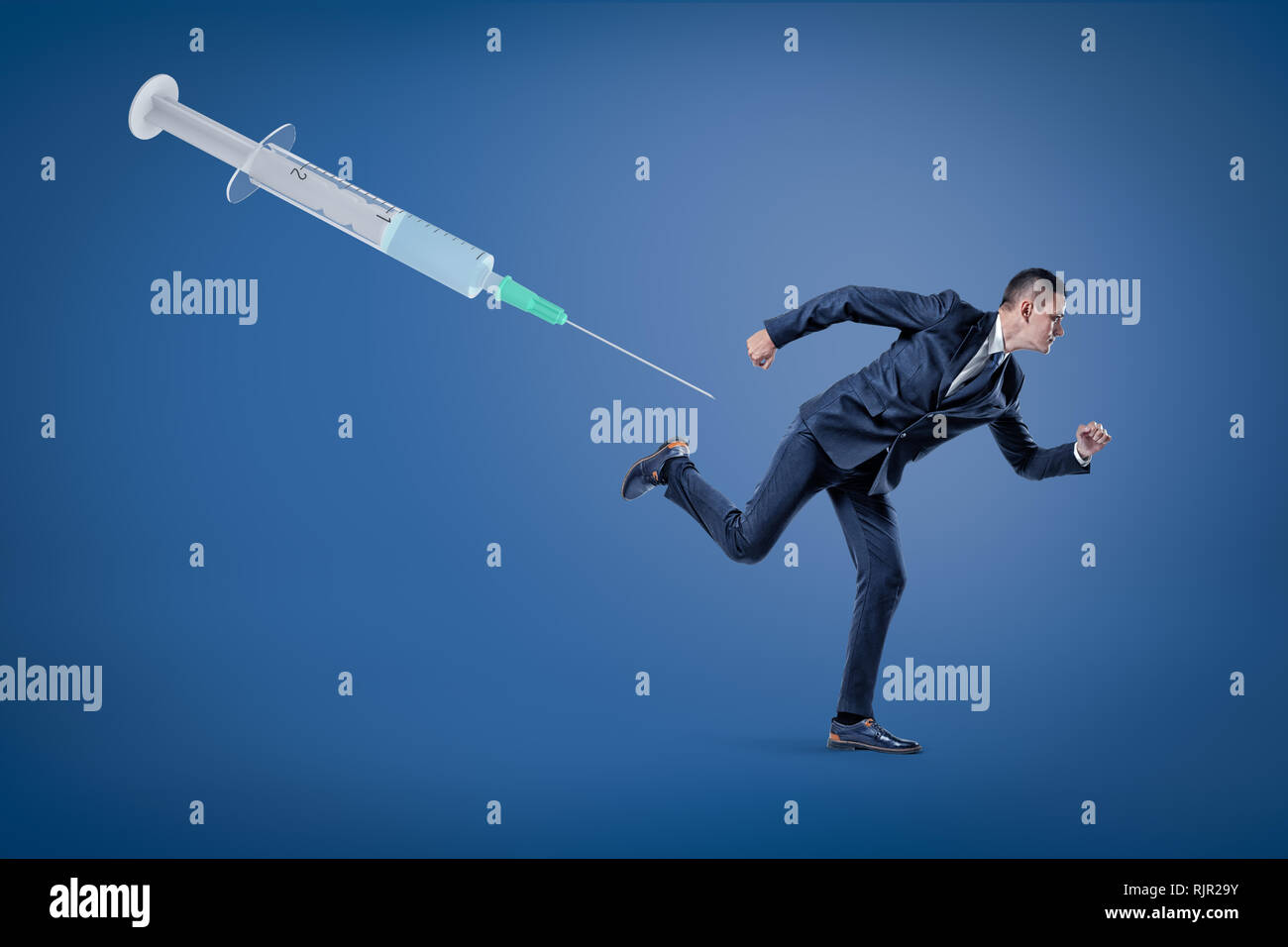 Una vista laterale di un imprenditore in esecuzione da un enorme siringa galleggianti in aria su uno sfondo blu. La paura di vaccini. Rifiuto di vaccini e la relativa d Foto Stock