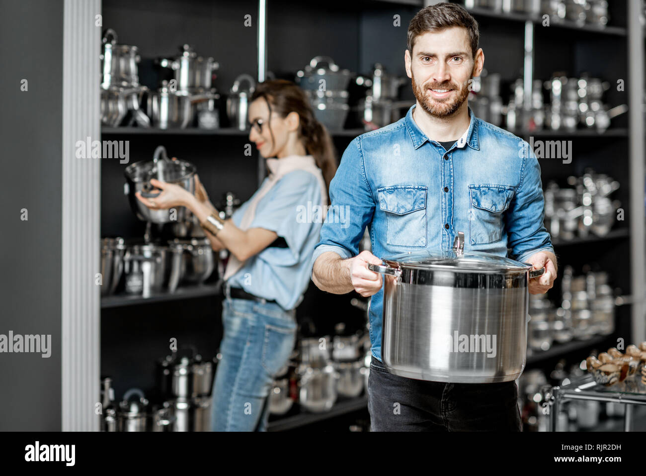 Coppia giovane scegliendo pentole per la cottura nel reparto con utensili da cucina al supermercato Foto Stock