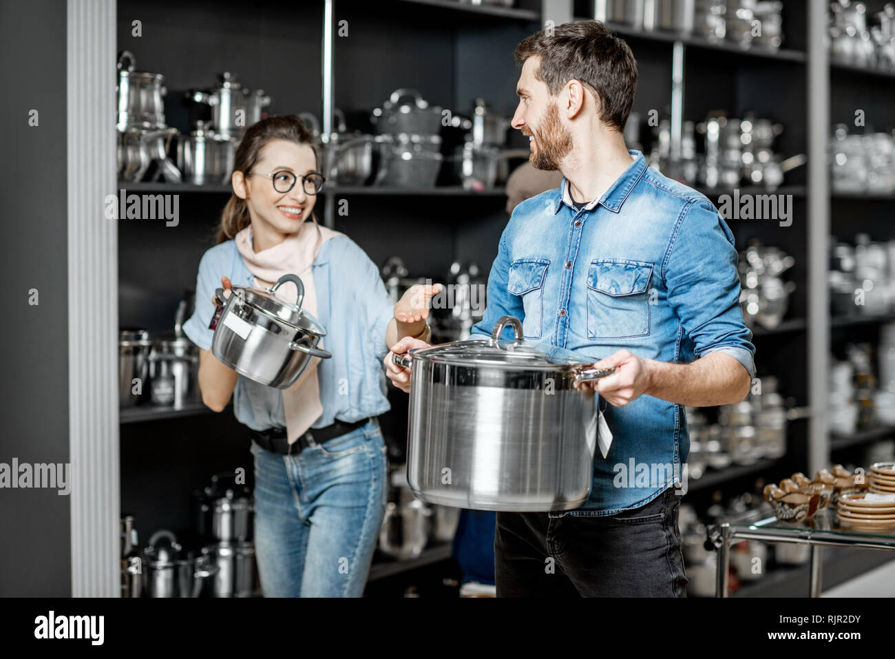 Coppia giovane scegliendo pentole per la cottura nel reparto con utensili da cucina al supermercato Foto Stock