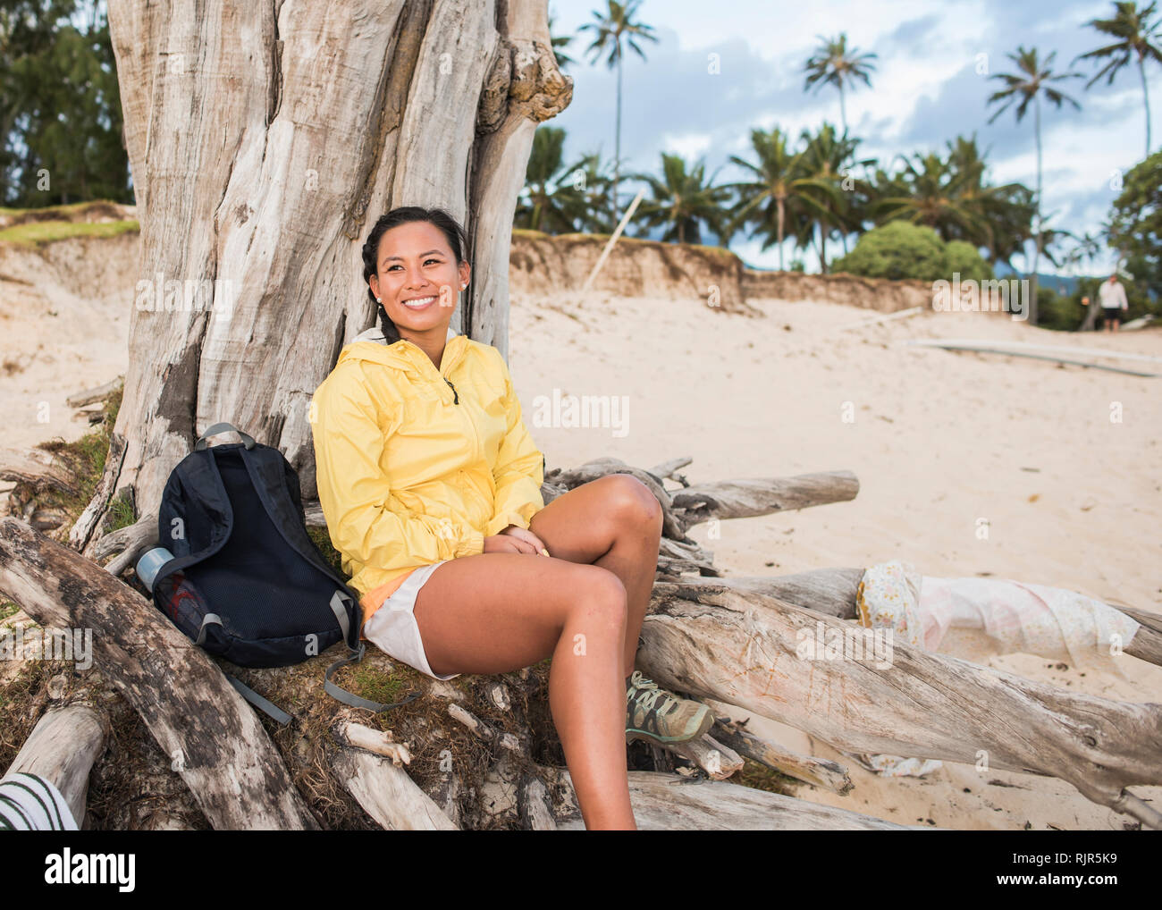 Donna rilassante dal vecchio albero tronco, Kailua Beach, Oahu, Hawaii Foto Stock