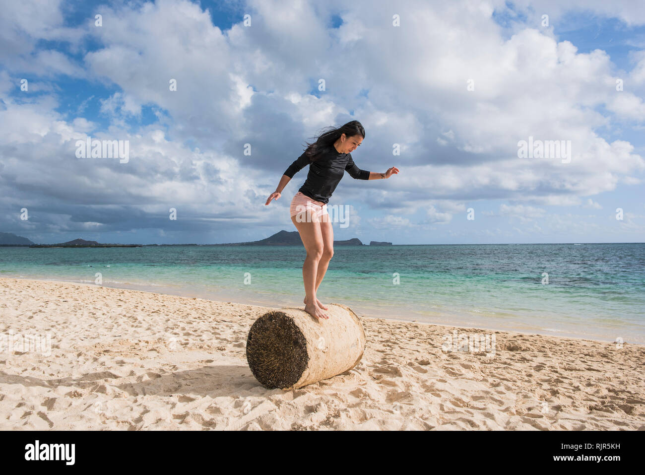 Donna in equilibrio su rotolo di erba, Lanikai Beach, Oahu, Hawaii Foto Stock