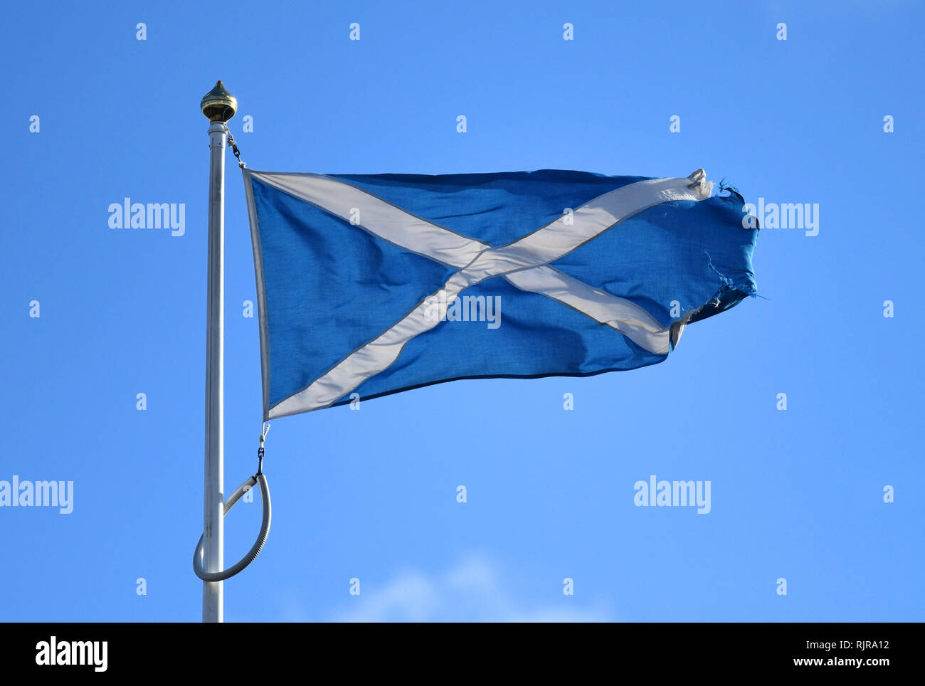 Un rip e lacerato e vecchia bandiera scozzese battenti contro un cielo blu a Edimburgo, Scozia. Foto Stock