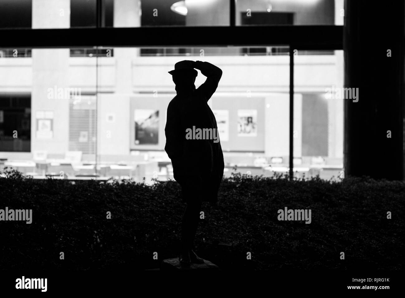 Statua di uomo apparentemente guardando deserte aprire uno spazio ufficio di notte Foto Stock