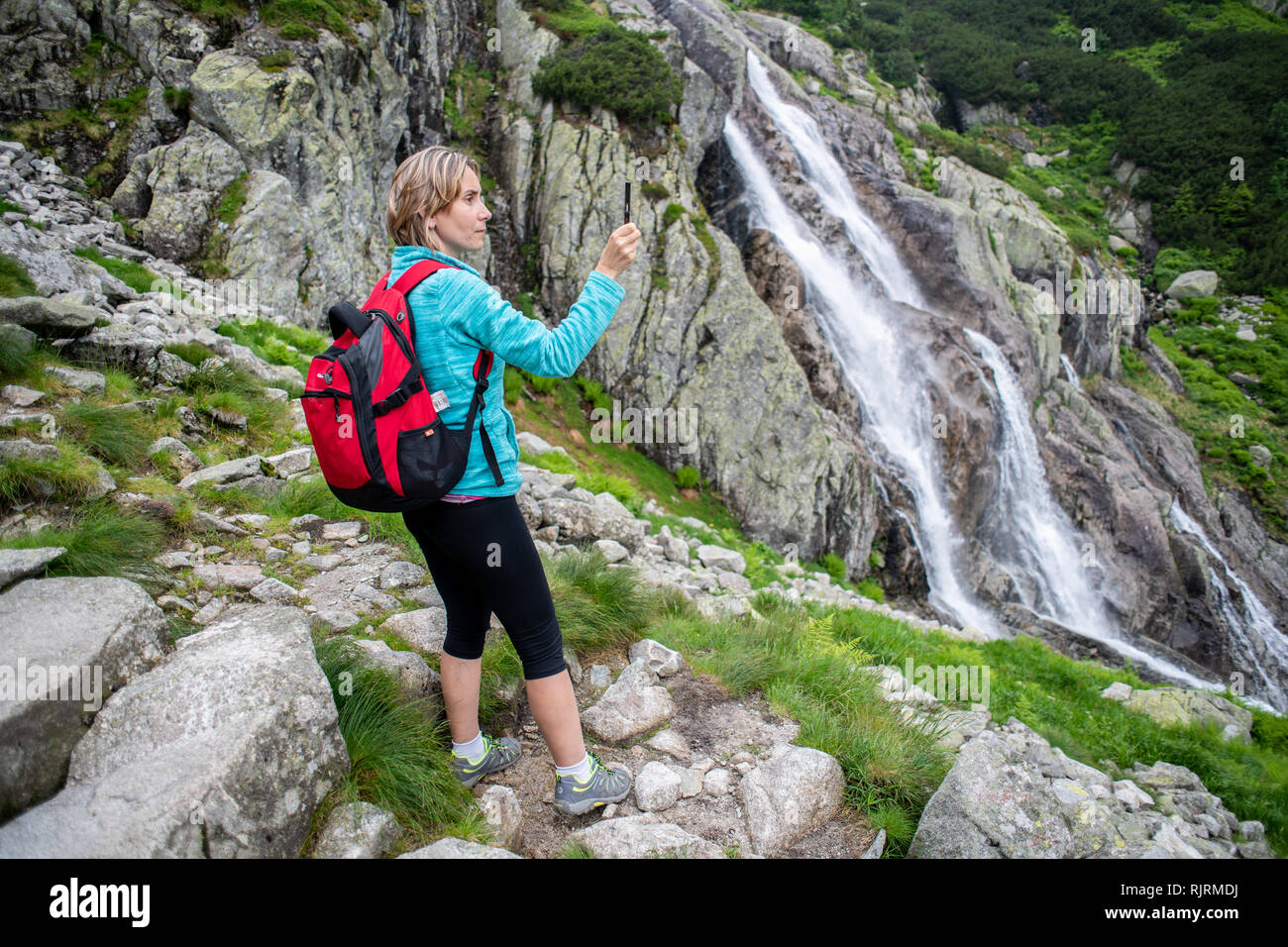 Una donna scatta una foto con il suo telefono cellulare della Wielka Siklawa la cascata più alta in Polonia nel Parco nazionale dei Tatra,Piccola Polonia voivodato, Polan Foto Stock