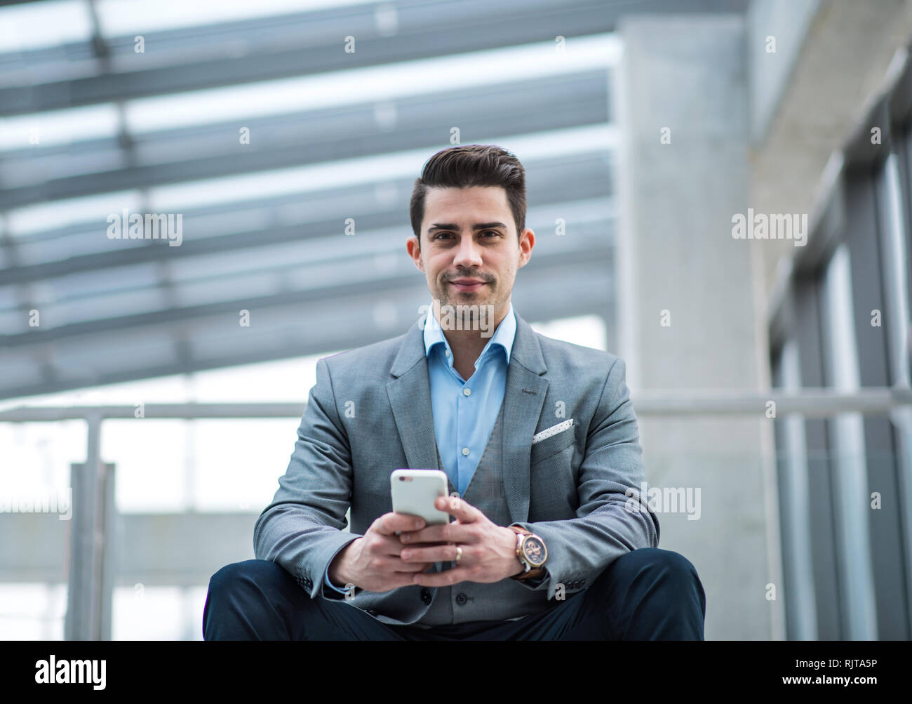 Un Ritratto di giovane imprenditore con seduta dello smartphone nel corridoio al di fuori ufficio. Foto Stock