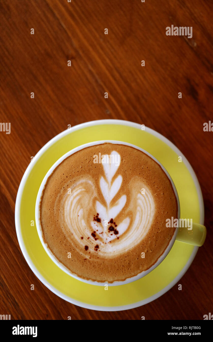Tazza di cappuccino caffè con latte art su un rosso marrone tavolo in legno Foto Stock