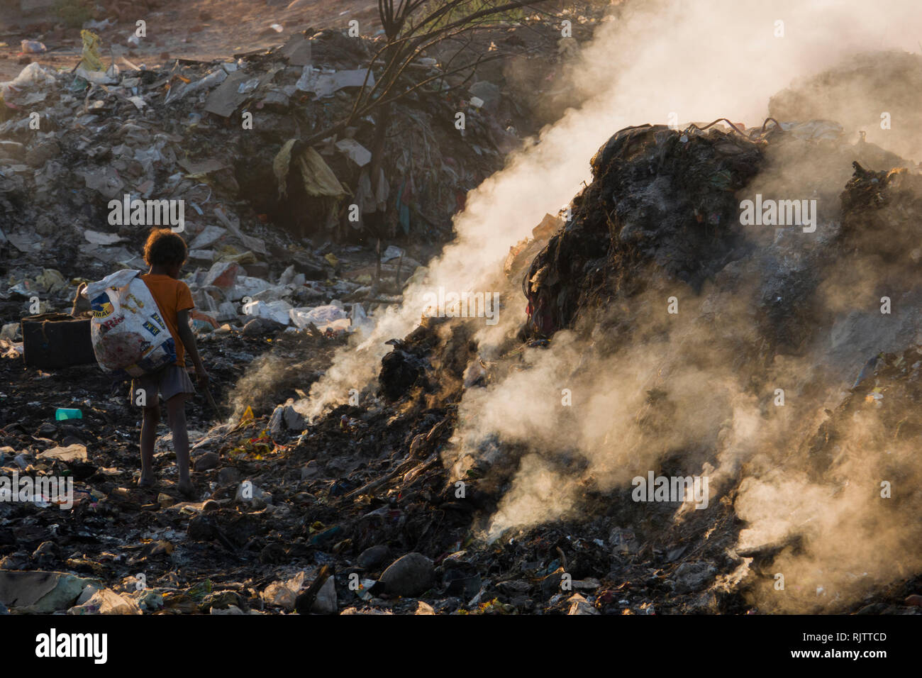 Un giovane bambino la raccolta di materiali riciclabili tra fumo tossico da discarica a Rishikesh, Uttarakhand, India Foto Stock