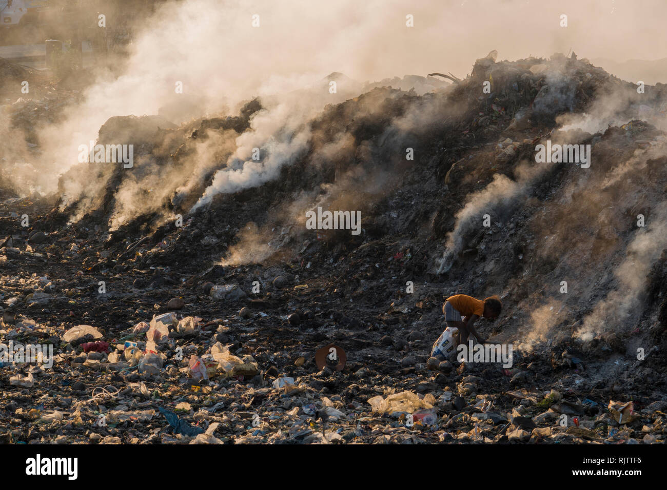 Un giovane bambino la raccolta di materiali riciclabili tra fumo tossico da discarica a Rishikesh, Uttarakhand, India Foto Stock