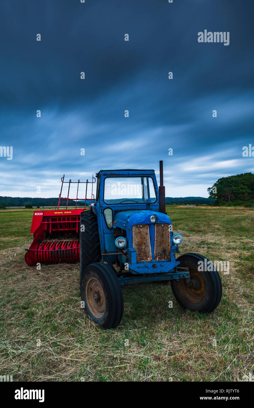Il rosso e il blu nel campo con il trattore con cielo tempestoso, Halland, Svezia, Europa Foto Stock