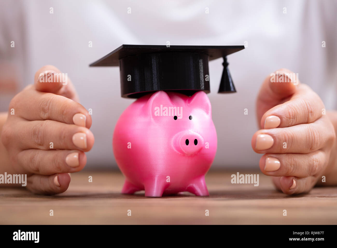 Close-up di una donna di mano la protezione di salvadanaio con graduazione il cappello sulla scrivania in legno Foto Stock