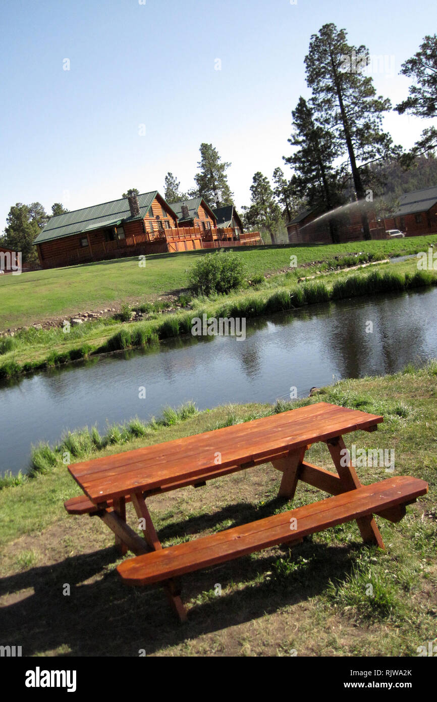 Un legno picknick tavolo siede accanto a un lago con cabine a distanza in Greer, Arizona. Foto Stock