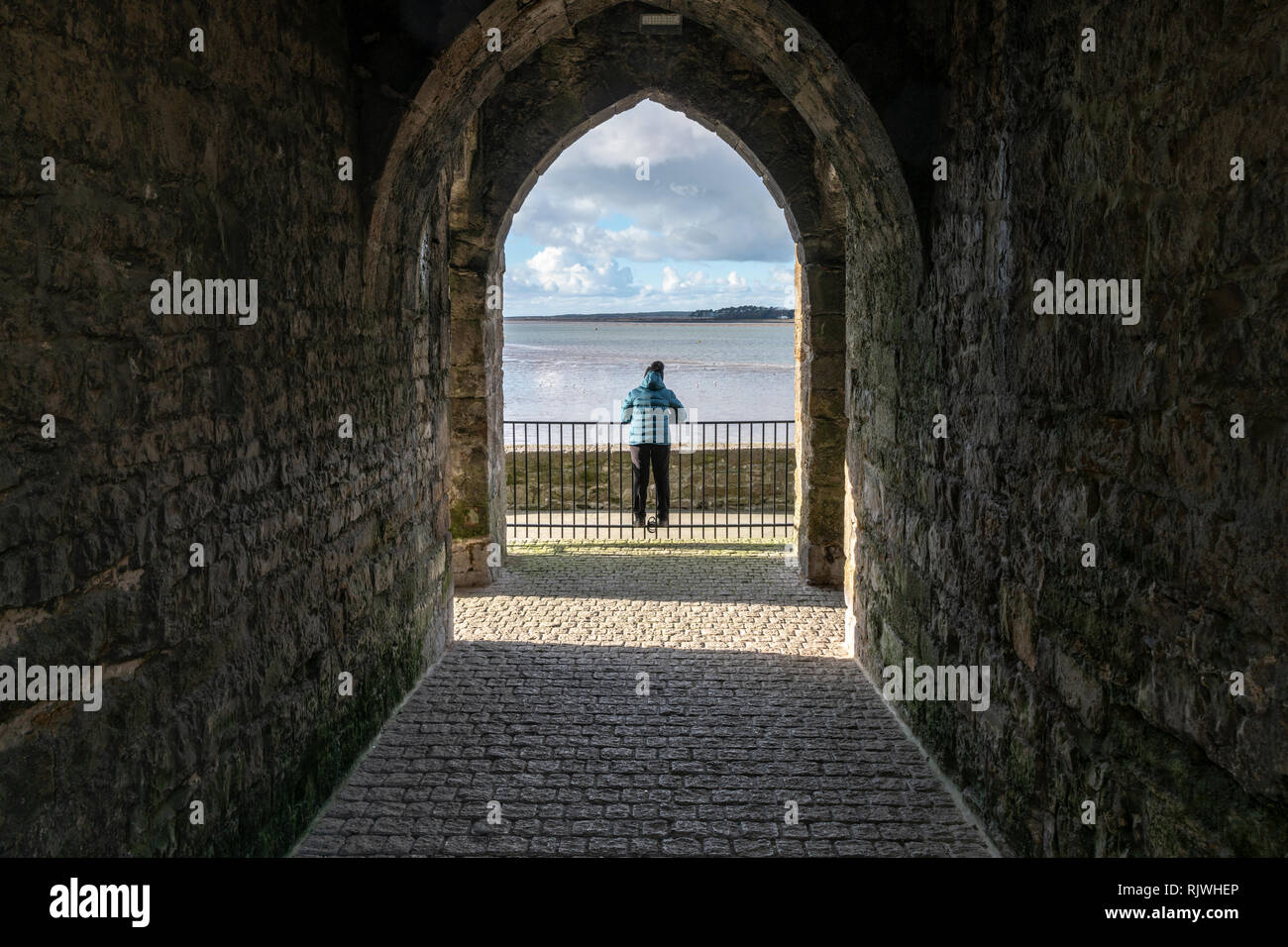 Una donna che guarda verso il Menai Straits nel Galles del Nord da un arco a Caernarfon. Foto Stock