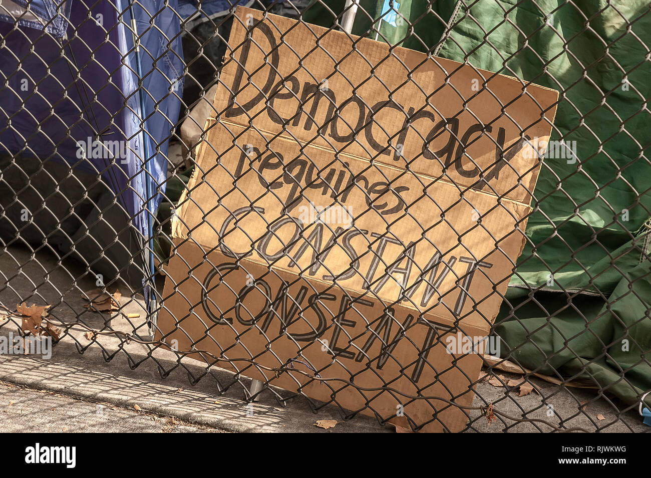Un segno politico dietro un recinto afferma che la democrazia richiede una costante consenso. Foto Stock