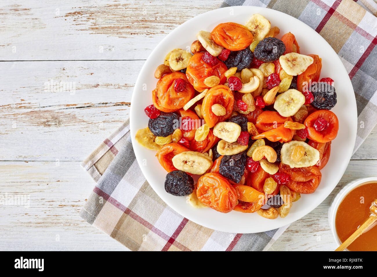 La frutta secca e il dado Mix bowl - fette di banana, albicocche, uva passa, prugne, ciliegie e anacardi su un tavolo rustico con il miele in una ciotola, vista orizzontale Foto Stock