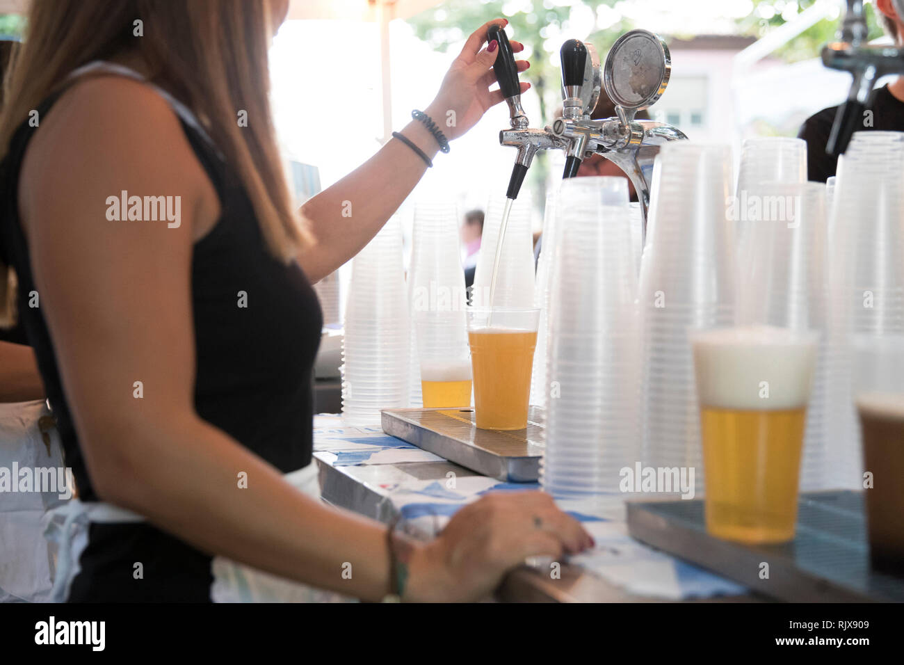 Primo piano di una giovane donna mentre sta lavorando in corrispondenza del rubinetto di birra e sta toccando una bionda la birra in un bicchiere di plastica durante una festa di primavera. Foto Stock