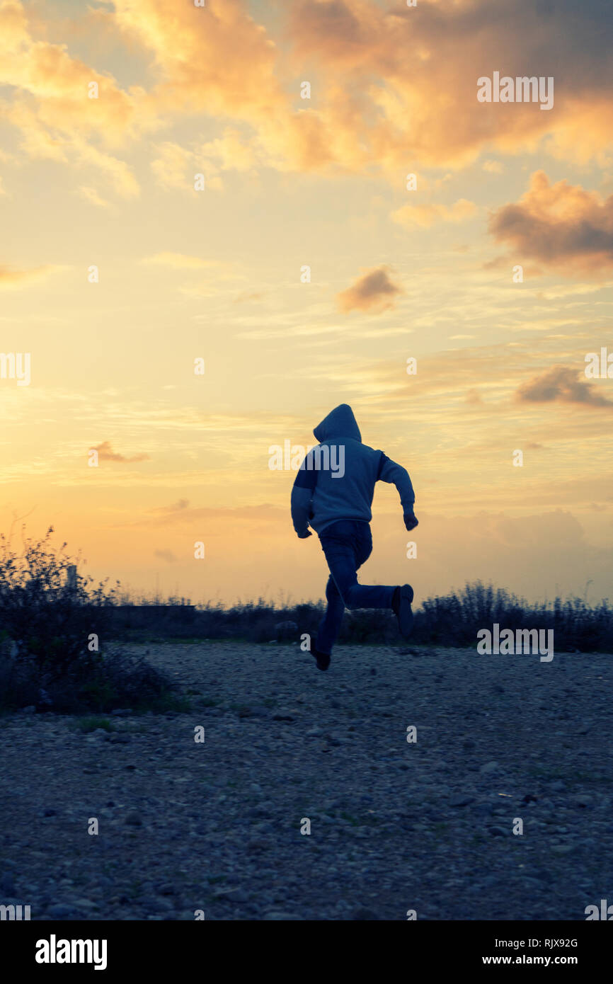 Misterioso uomo incappucciato scappando al tramonto Foto Stock