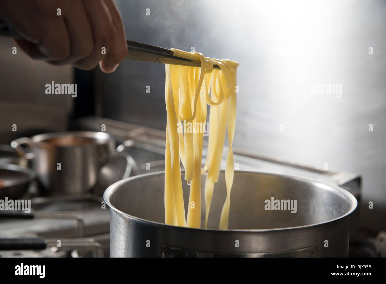 Primo piano di uno chef con pinze in mano ha il controllo tagliatelle in ebollizione in una pentola. Egli è in una cucina professionale. Foto Stock