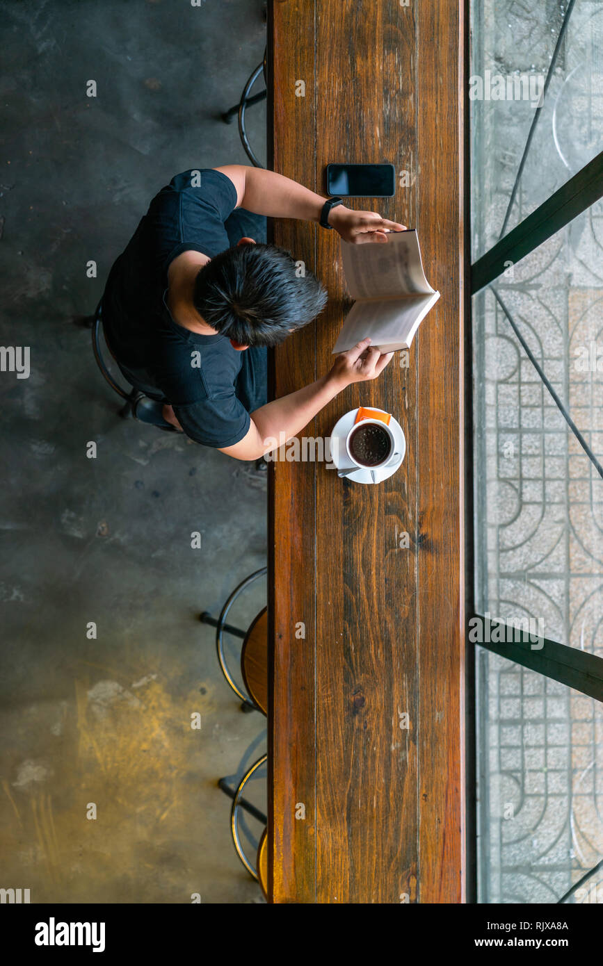 Uomo asiatico la lettura di libri e di bere il caffè Foto Stock