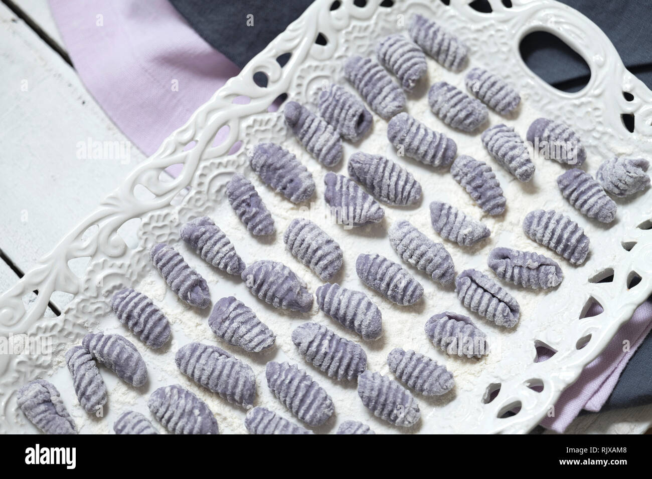 Inquadratura orizzontale di materie gnocchi viola su un bianco porcellana vintage vassoio. Violetta italian gnocchi fatti con patate viola. Foto Stock