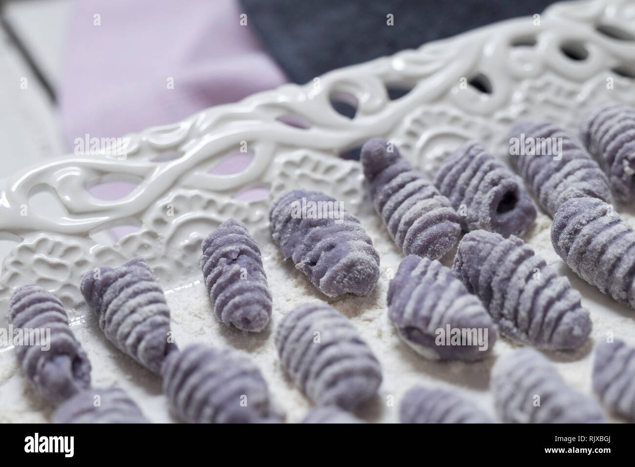 Vista frontale colpo di materie gnocchi viola su un bianco porcellana vintage vassoio. Violetta italian gnocchi fatti con patate viola. Foto Stock