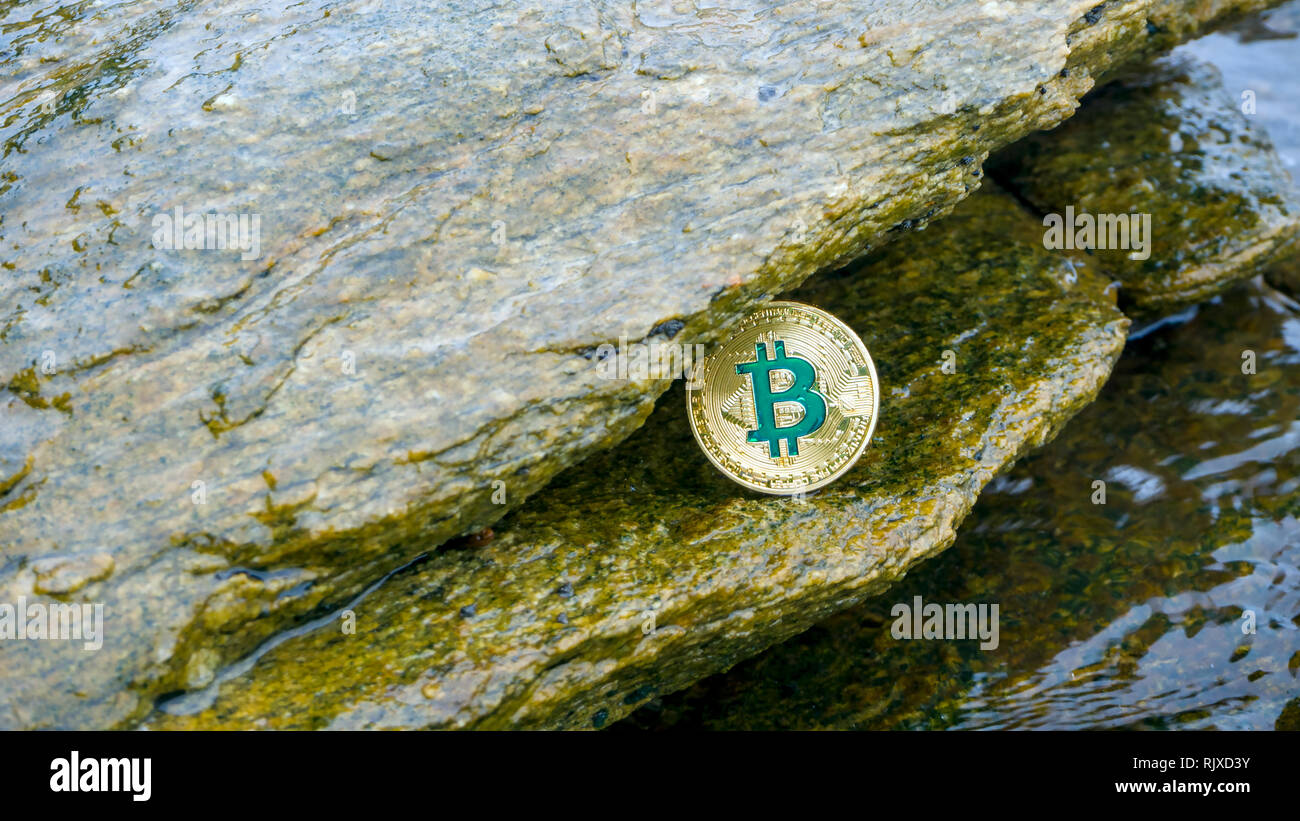 La moneta in oro di Bitcoin risiede nella roccia con le onde del mare. Bitcoin è un moderno modo di scambiare questo crypto moneta è un comodo mezzo di pagamento da me Foto Stock