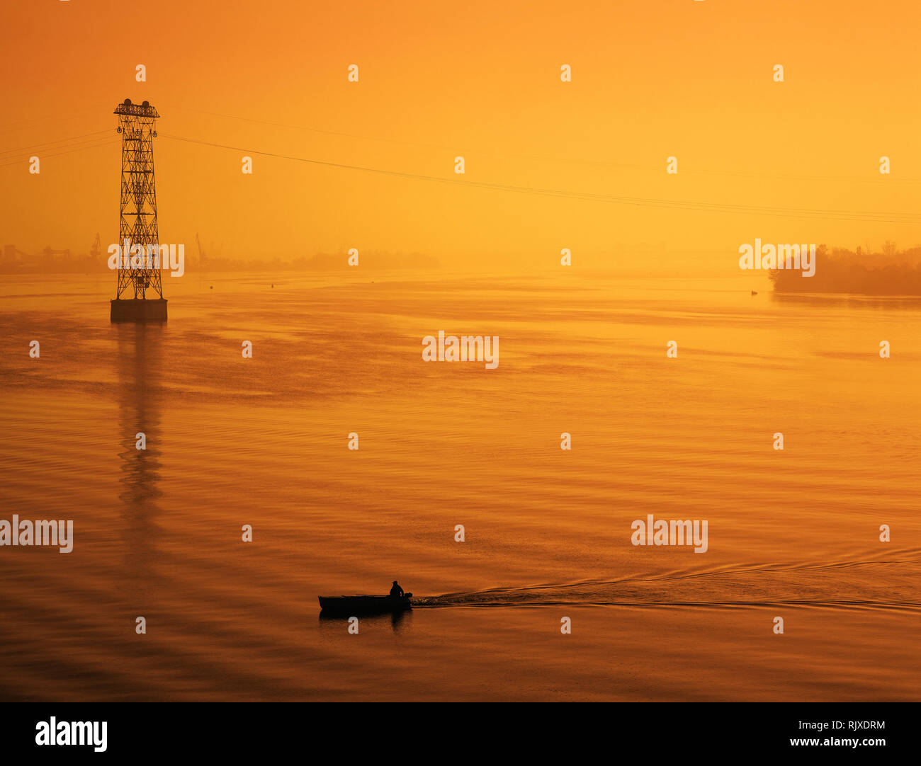 Paesaggio industriale, pescatore su una barca al tramonto Foto Stock