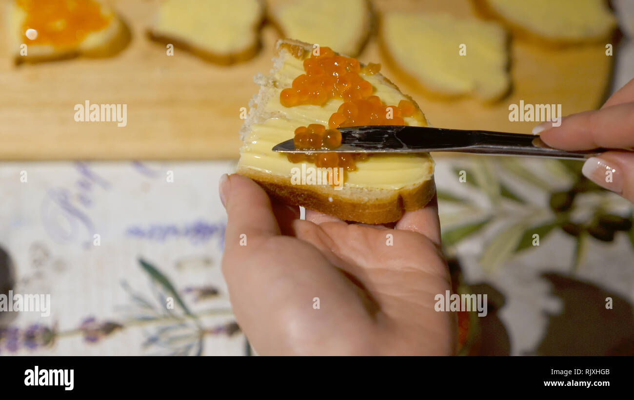 Mani femminili si diffonde caviale rosso con il coltello sul pane con burro per party spuntini Foto Stock