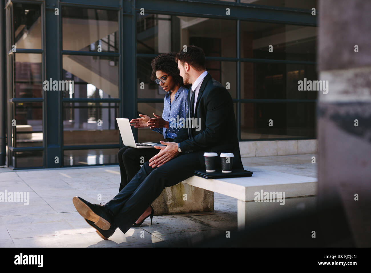 Due persone di affari seduta su una panchina in un ufficio moderno edificio con un computer portatile. Donna con notebook discutere di affari con il collega di sesso maschile. Foto Stock