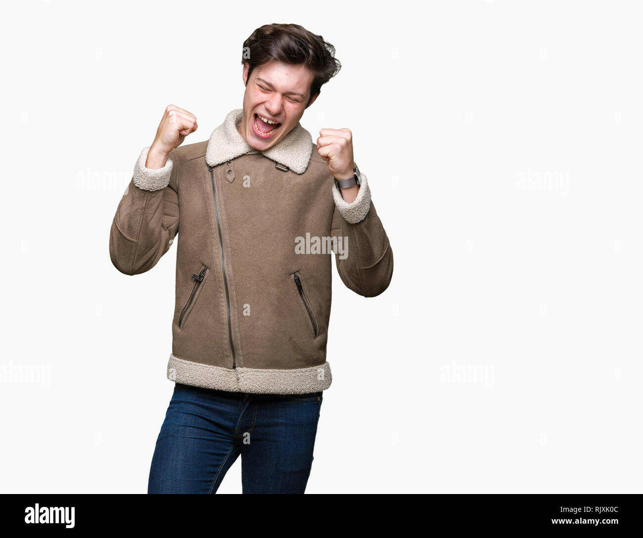 Giovane uomo bello indossare cappotto invernale su sfondo isolato molto felici ed eccitati facendo vincitore gesto con le braccia sollevate, sorridente e urlando fo Foto Stock