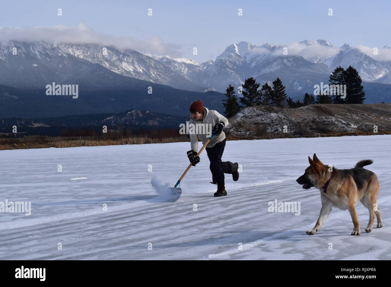 Un uomo si cancella la neve fuori all'aperto una pista di pattinaggio su un laghetto nei pressi Invermere, BC, nelle Montagne Rocciose Canadesi Foto Stock