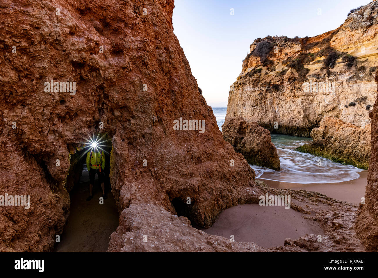 Uomo che indossa il proiettore sotto arco naturale di roccia, Alvor, Algarve, Portogallo, Europa Foto Stock
