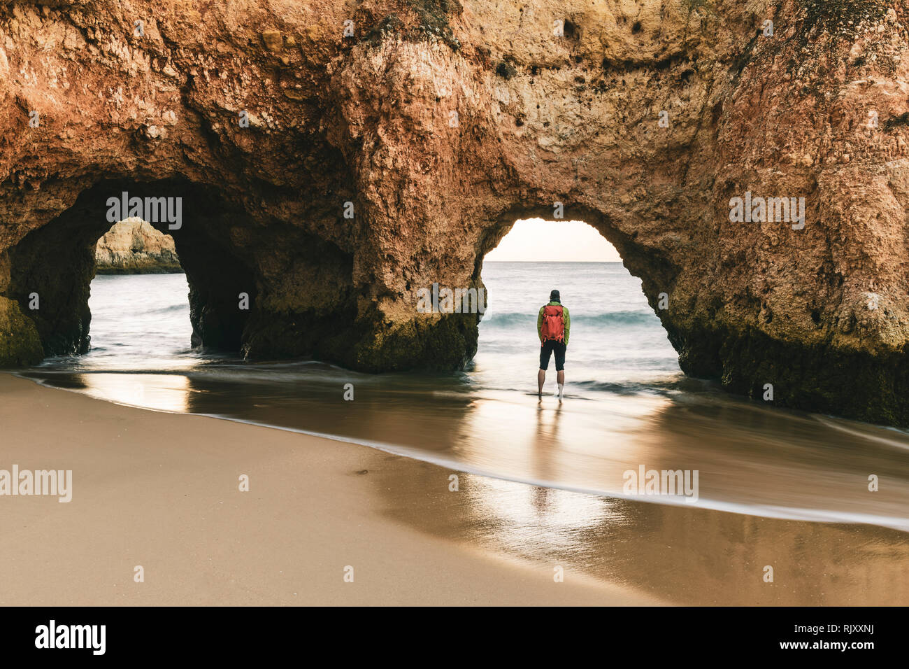 L'uomo esplorare scogliere e formazioni rocciose da bordo d'acqua, Alvor, Algarve, Portogallo, Europa Foto Stock