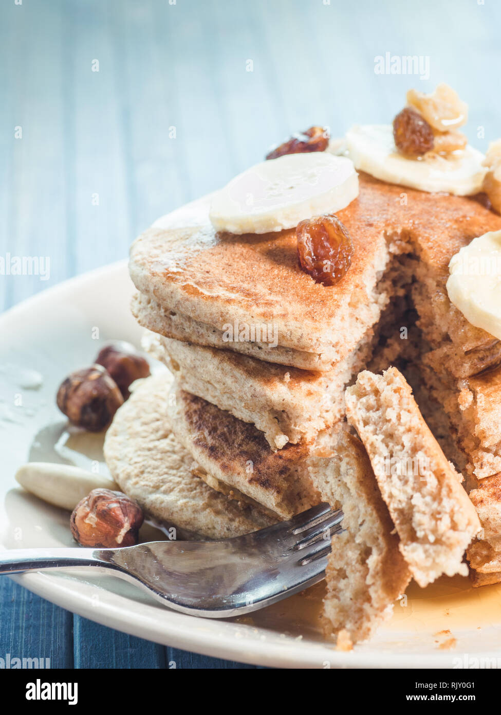 Mangiare con il fork di un grano intero pancake con banane fresche ,uva passa e noci, miele . sana colazione con frutta e noci Foto Stock