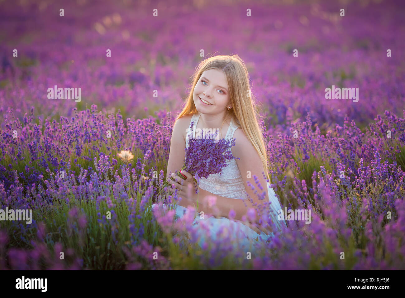 Sorridente bella bionda signora modello sul campo di lavanda godere giorno di estate indossa ariosa abito di Pentecoste con bouquet di fiori Foto Stock