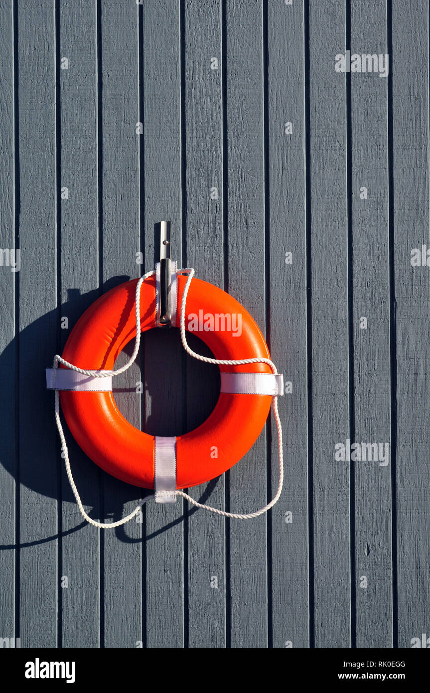 Un arancio salvagente appeso ad un muro grigio di una boathouse Foto Stock