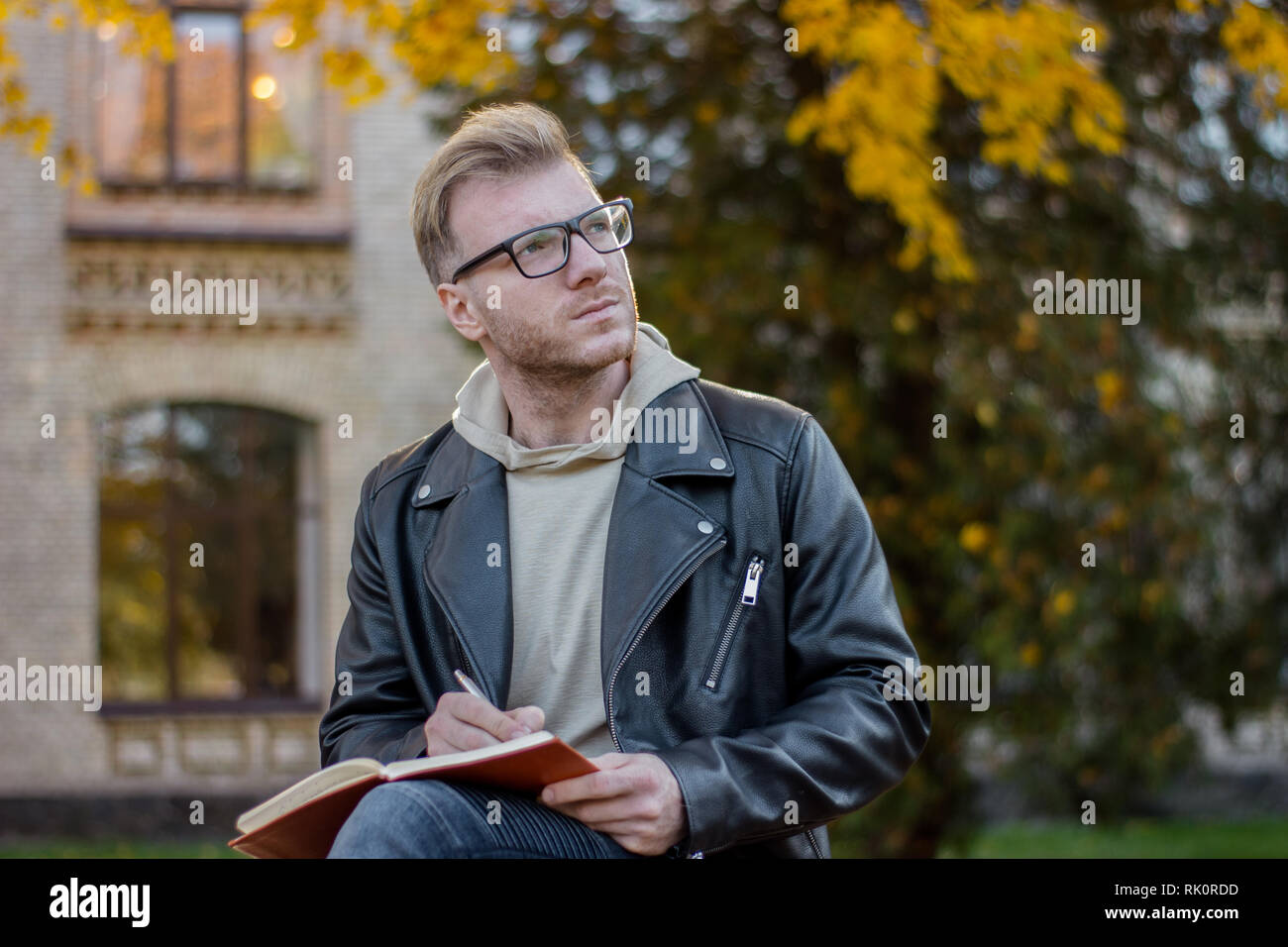 Ritratto di sognare smart guy scrittore in abiti casual rende note in un notebook e si siede su una panchina nel parco Foto Stock
