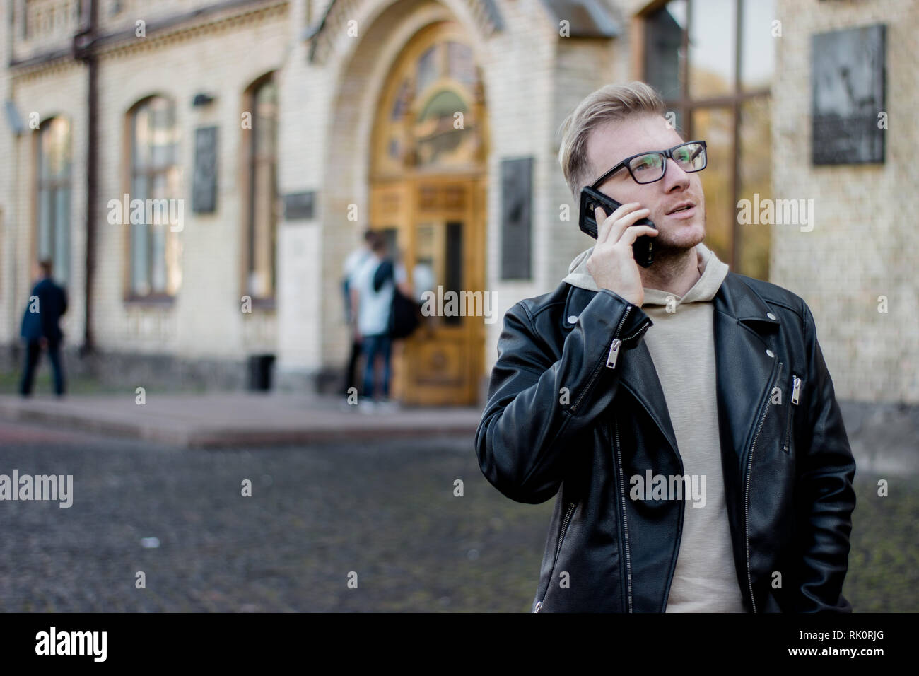 Dreaming smart guy è parlare al telefono mentre è in piedi vicino all'università di spazio di copia Foto Stock