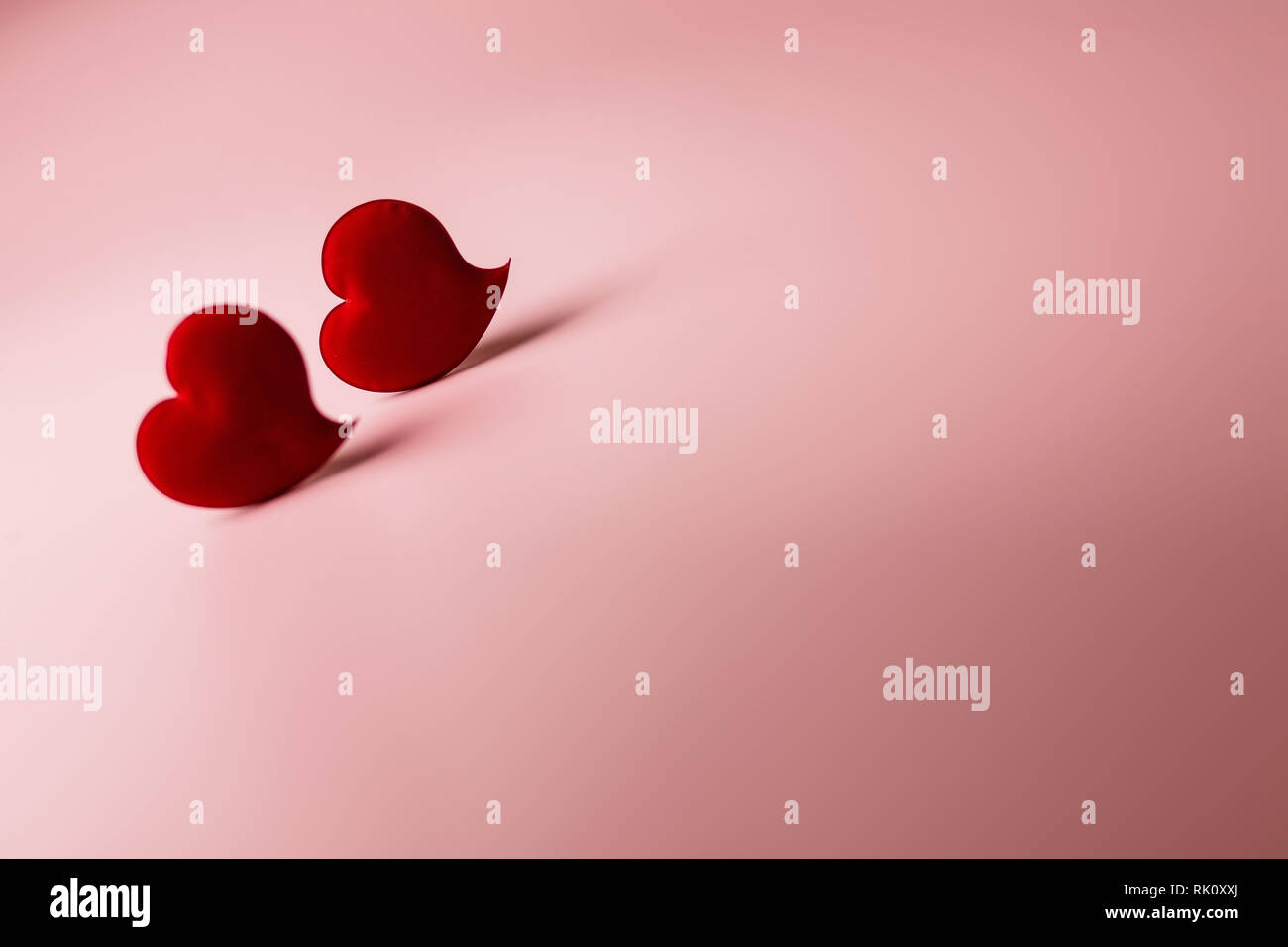 Due velluto rosso a cuori in soft focus su uno sfondo di colore rosa. Sfondo con copia spazio per il giorno di San Valentino o matrimoni Foto Stock