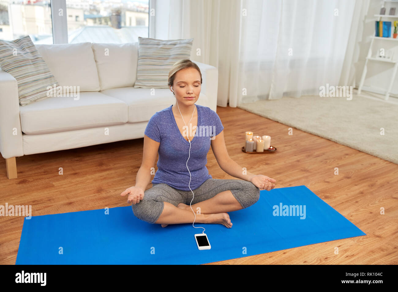 Donna con la musica sullo smartphone meditando a casa Foto Stock