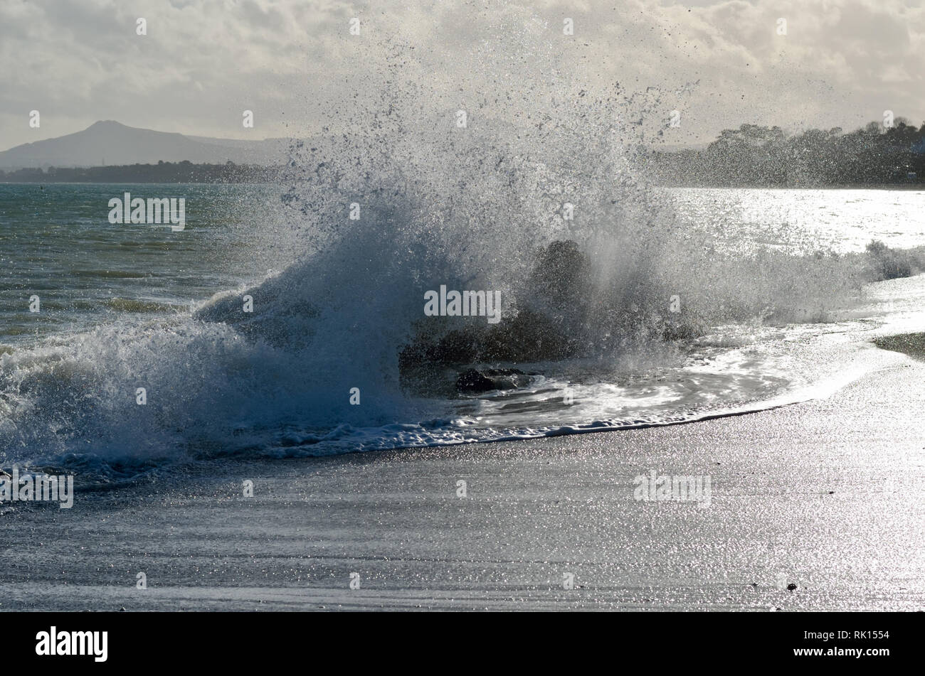 Onde infrangersi su rocce sulla spiaggia di killiney,Dublino,l'Irlanda,illuminata dal sole,azionato da potenti venti onshore. Foto Stock