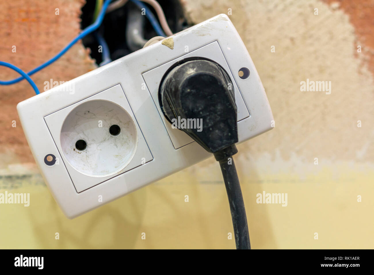 Presa di alimentazione doppia presa con il collegamento elettrico di isolati fili colorati, tappo di plastica installazione su luce gialla parete intonacata. Home interio Foto Stock