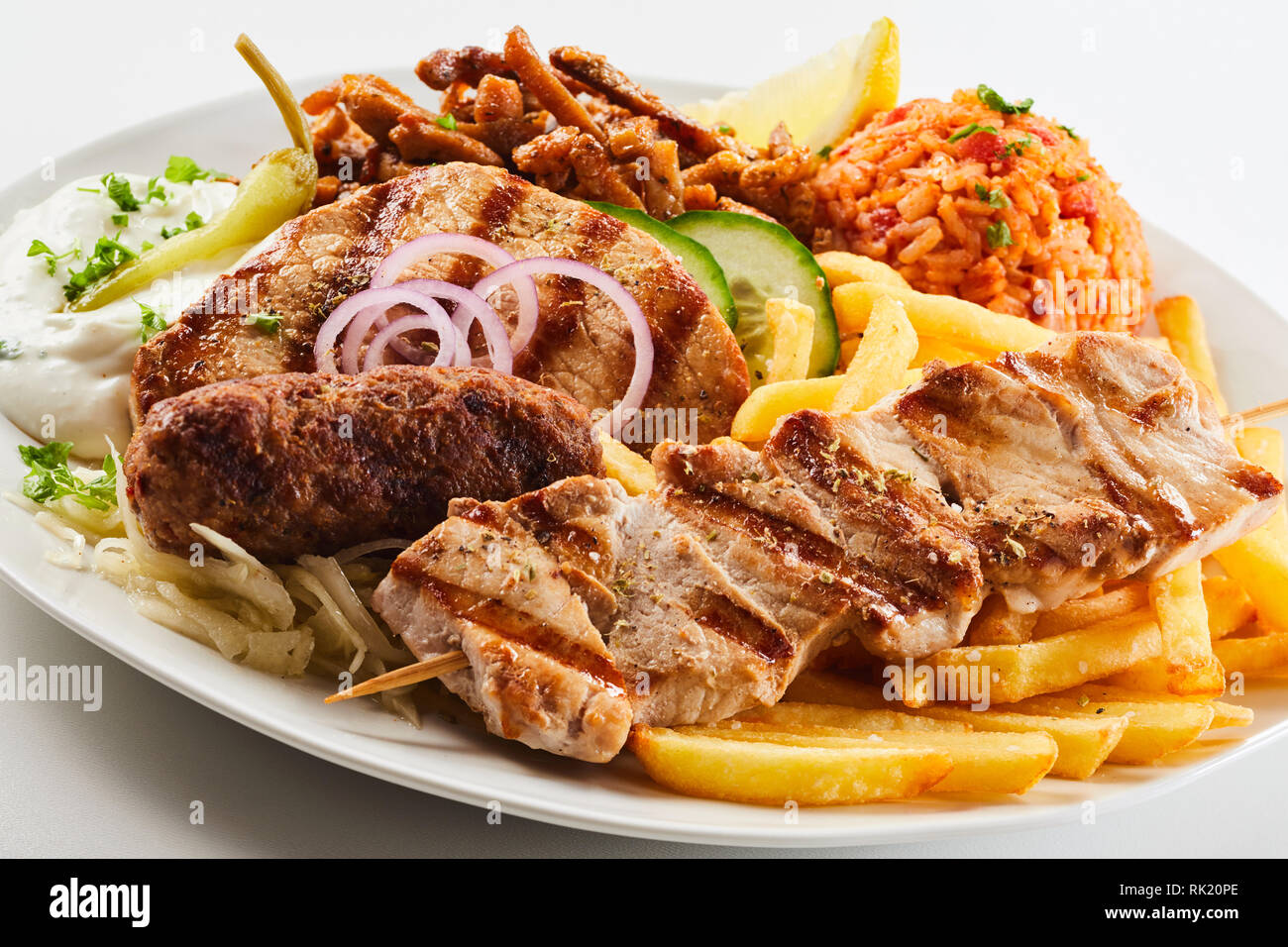 Un assortimento di grigliate di carne con patate fritte chips, saporito il riso e insalata servita su una piastra in una vista ravvicinata del regionale cucina greca Foto Stock