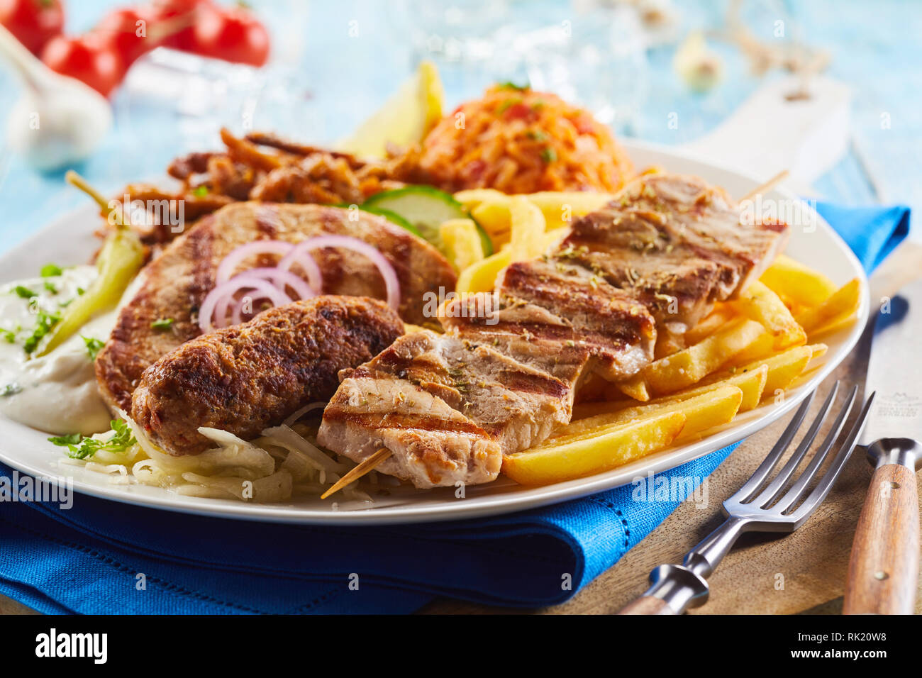 Grigliate di carni assortite su una piastra con fried potato chips, saporita, riso, insalata e anelli di cipolla per una gustosa cena greca in una vista ravvicinata Foto Stock