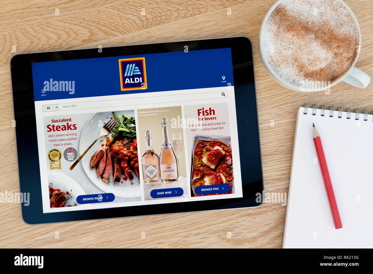 Il sito web di Aldi funzioni su un iPad dispositivo tablet pc che si appoggia su una tavola di legno accanto a un blocco note (solo uso editoriale). Foto Stock