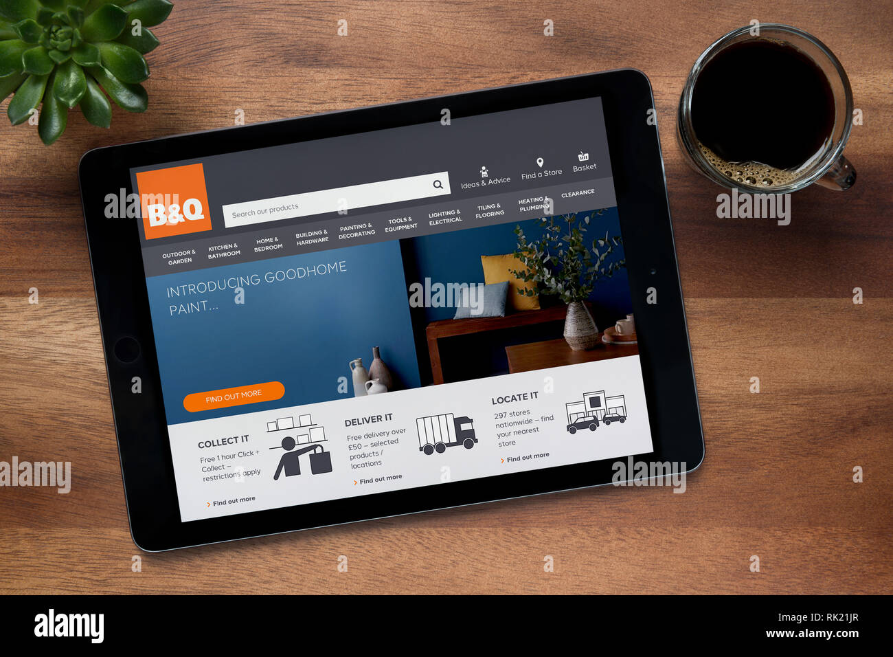 Il sito del B&Q è visto su un tablet iPad, su di un tavolo di legno lungo con un caffè espresso e una pianta di casa (solo uso editoriale). Foto Stock
