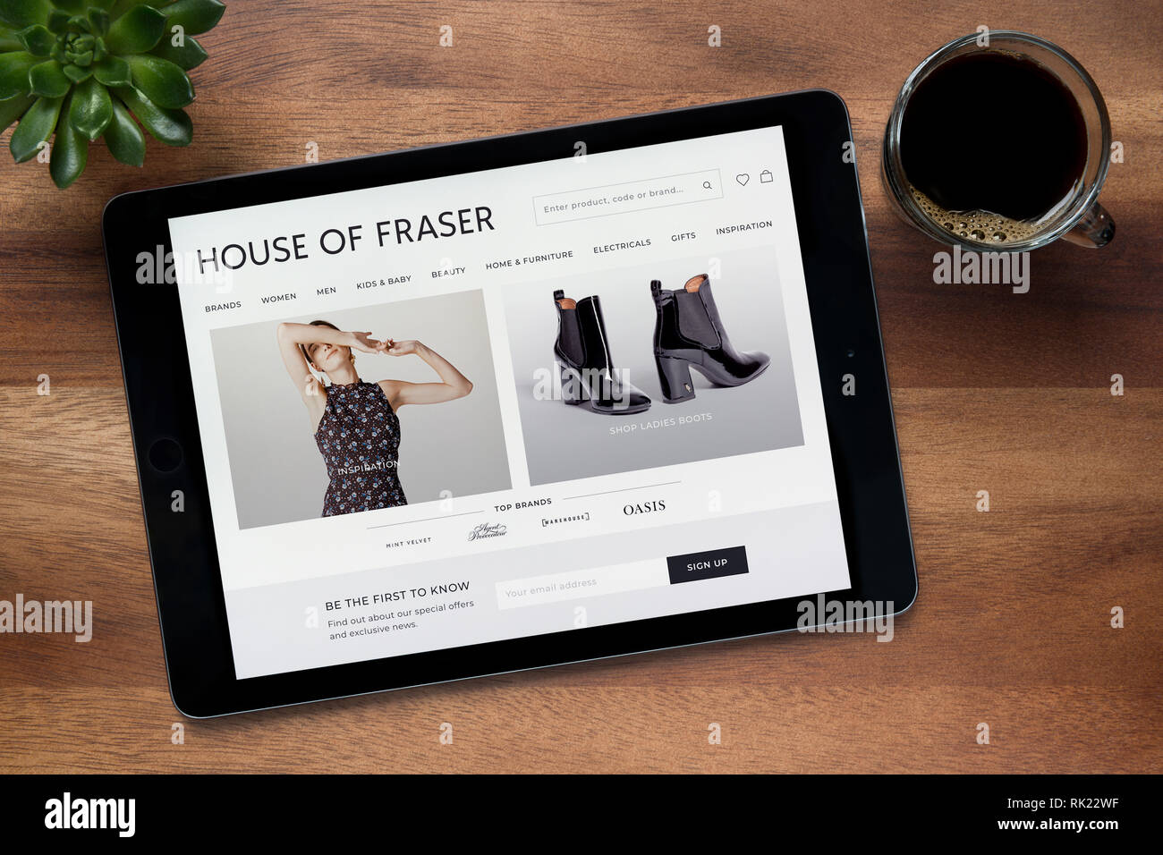 Il sito web di House of Fraser è visto su un tablet iPad, su di un tavolo di legno lungo con un caffè espresso e una pianta di casa (solo uso editoriale). Foto Stock