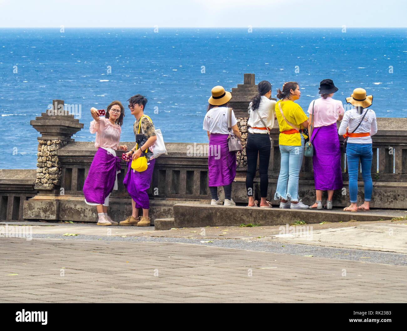 I turisti cinesi indossando viola sarong visitando il Tempio Uluwatu Bali Indonesia. Foto Stock