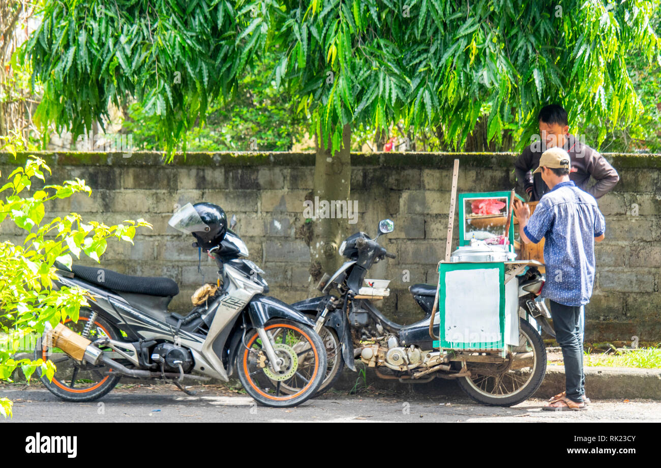 La vita quotidiana, l'uomo l'acquisto di cibo da un venditore ambulante Jimbaran, Bali Indonesia. Foto Stock