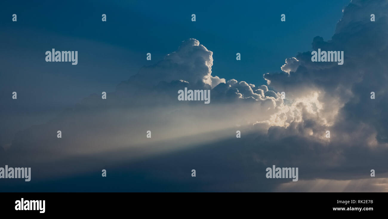 Bella e soleggiata la mattina presto il cielo blu di sfondo morbido con raggi di sole tra bianchi e soffici enorme nube. Orizzontale fotografia a colori. Foto Stock