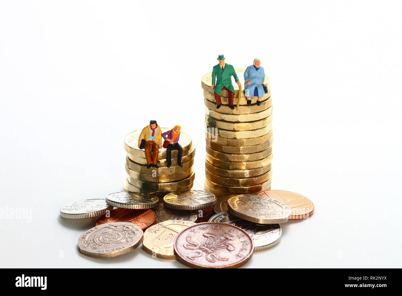 Diorama concettuale immagine di una figura in miniatura pensionati coppia e. la giovane coppia sedette su una pila di monete da sterline Foto Stock